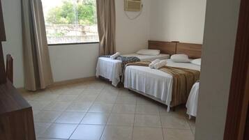 A hotel room with two beds, a window with curtains, a wooden headboard, and a tiled floor.