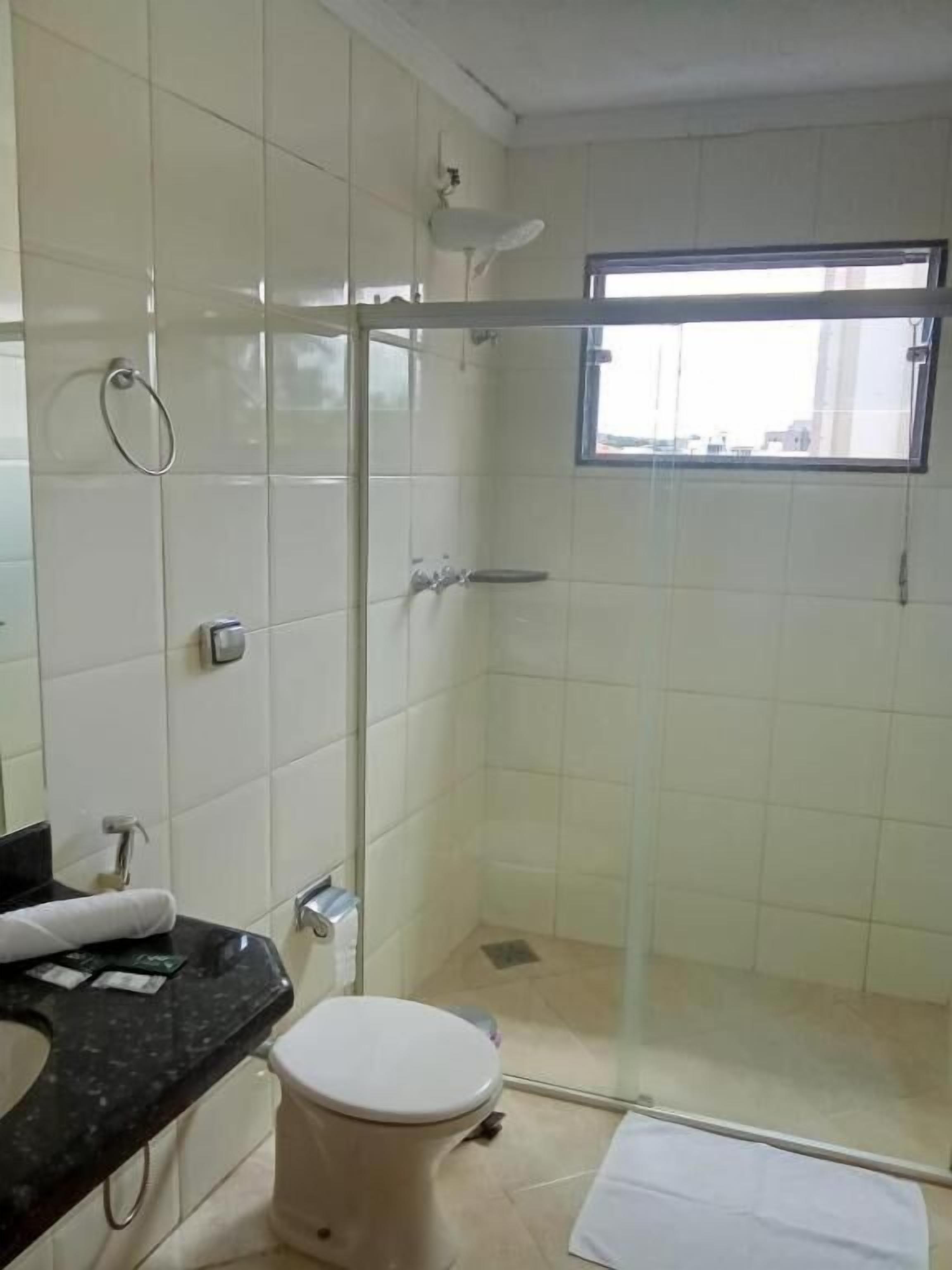Un baño con inodoro, lavamanos, ducha con puerta de vidrio y ventana.