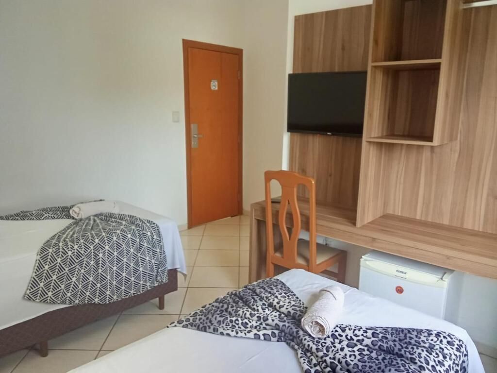 Een hotelkamer met twee bedden, een houten garderobe, een televisie en een bureau met een stoel.