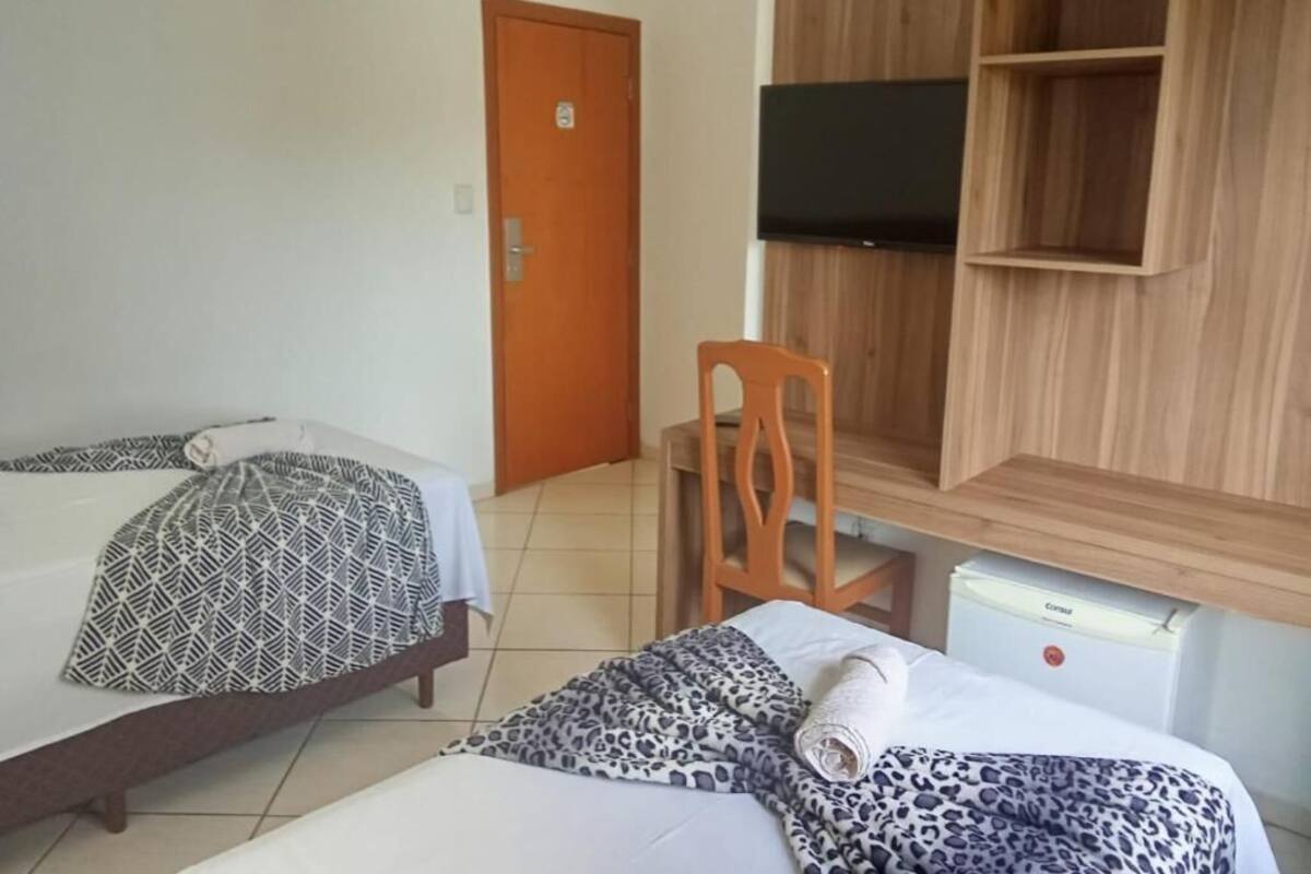 Een hotelkamer met twee bedden, een houten garderobe, een televisie en een bureau met een stoel.