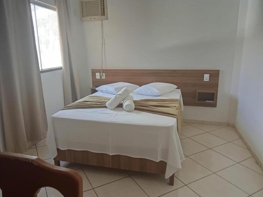 Een net opgemaakt bed met witte lakens en een handdoek, een houten hoofdbord en een klein nachtkastje met een lamp.