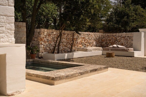 Un espace piscine agrémenté de murs en pierre, d’un coin salon extérieur blanc et d’une plante en pot.