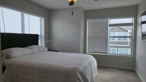 Ein Schlafzimmer mit einem Bett, einem Nachttisch, einer Deckenleuchte und einem Fenster mit Jalousien.