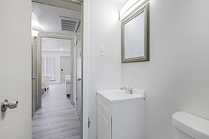 Un corridoio stretto che conduce a un bagno con lavandino e specchio bianchi.