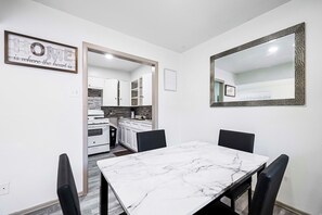 Zona pranzo con tavolo in marmo e sedie nere, cucina sullo sfondo e uno specchio a parete.