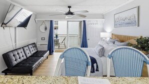 Ein modernes Hotelzimmer mit einer schwarzen Ledersofa, einem Bett mit blau-weißen Kopfhörern, einem Deckenventilator und Blick auf den Balkon.