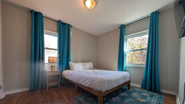 Un dormitorio con una cama de madera, un tapete azul estampado y cortinas azul verdosas.