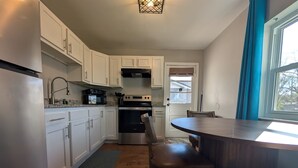 Una cocina con armarios blancos, un microondas, una estufa y un comedor con un banco.