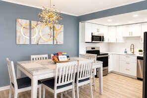 A modern kitchen with white cabinets, a stainless steel refrigerator, and a dining area with a table and chairs. - 20th-Floor Oceanfront Condo with Balcony, Pools, Beach Access & Resort Amenities (Ocean City)