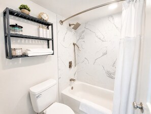 A bathroom with a white toilet, a bathtub with a showerhead, and marble-patterned walls. - 20th-Floor Oceanfront Condo with Balcony, Pools, Beach Access & Resort Amenities (Ocean City)