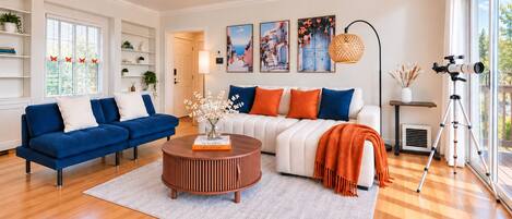 A modern living room with a blue sofa, a white sofa, and a round coffee table. There are paintings on the wall and a telescope on a stand.