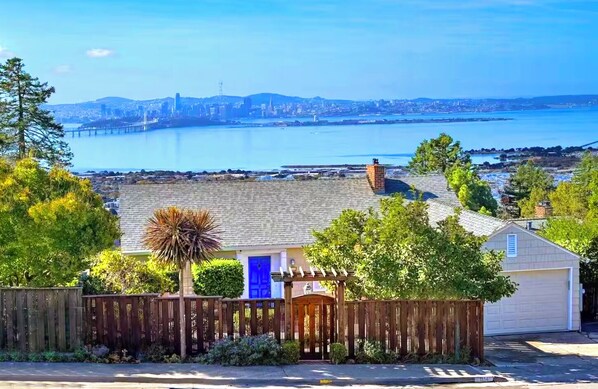 Ein Wohngebiet mit einem Haus, das eine blaue Tür, einen Holzzaun und einen Blick auf eine Stadtlandschaft über dem Wasser hat.
