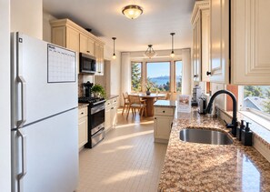 A modern kitchen with a refrigerator, stove, and microwave. There is a dining area with a table and chairs. The kitchen has a large window with a view of the city.