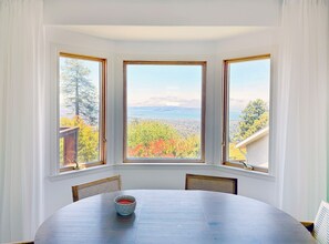 A dining area with a table and chairs, three windows with a view of trees and a bridge, and a bowl of red liquid on the table. - Cozy Berkeley Hills Home with Stunning Views (Berkeley)