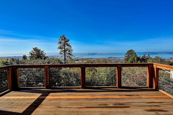 A wooden deck with a metal railing overlooking a cityscape and a body of water.