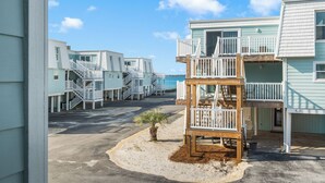 A beachfront property with multiple buildings, including a wooden deck with a staircase and a small palm tree. - Boardwalk A18 | Beach Access & Pool | New Listing! (Pensacola Beach)