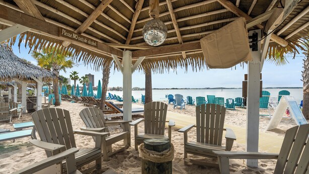 A beachside lounge with wooden chairs and a thatched roof. - Boardwalk A18 | Beach Access & Pool | New Listing! (Pensacola Beach)