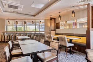 Un restaurante con mesas y sillas, un ventanal grande y lámparas colgantes.