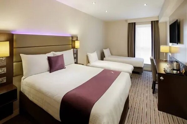 Habitación de hotel con dos camas, un escritorio, un televisor y un ventanal con cortinas.