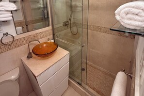 A bathroom with a glass-enclosed shower, a wooden bowl sink, and a glass shelf with a towel.