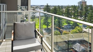 A balcony with a chair and table, overlooking a cityscape with buildings and greenery.