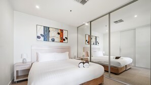 A modern bedroom with a large bed, a nightstand, a bedside table, a mirror, and abstract art on the wall.