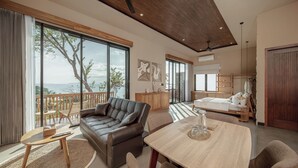 Ein modernes Wohnzimmer mit großem Fenster, einer Couch, einem Esstisch und Blick auf den Ozean.