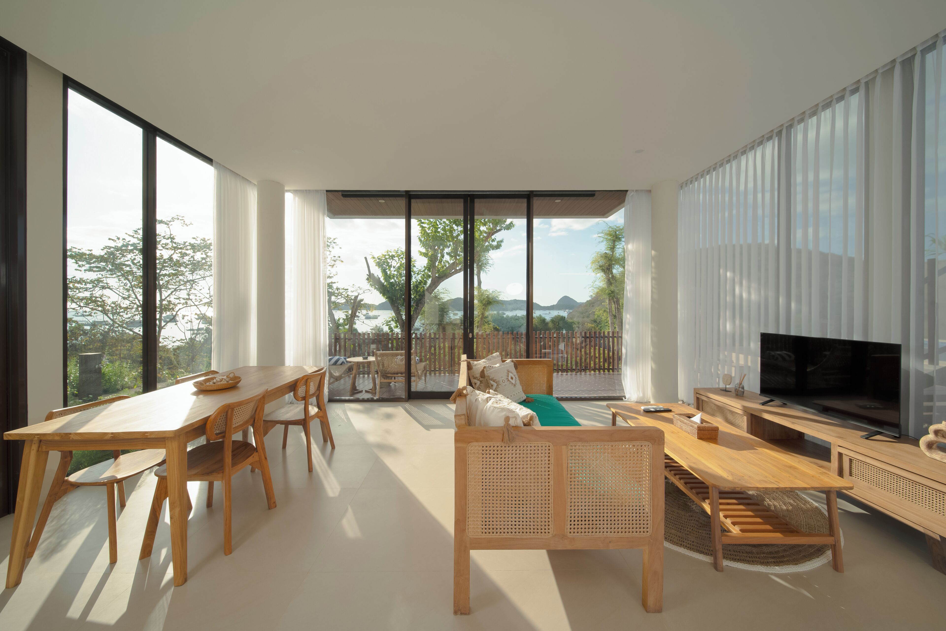 A spacious living area with a large TV, wooden furniture, and a balcony with a view of the landscape.