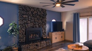 Ein Wohnzimmer mit Kamin aus Stein, Deckenventilator, Fernseher und einer Couch.