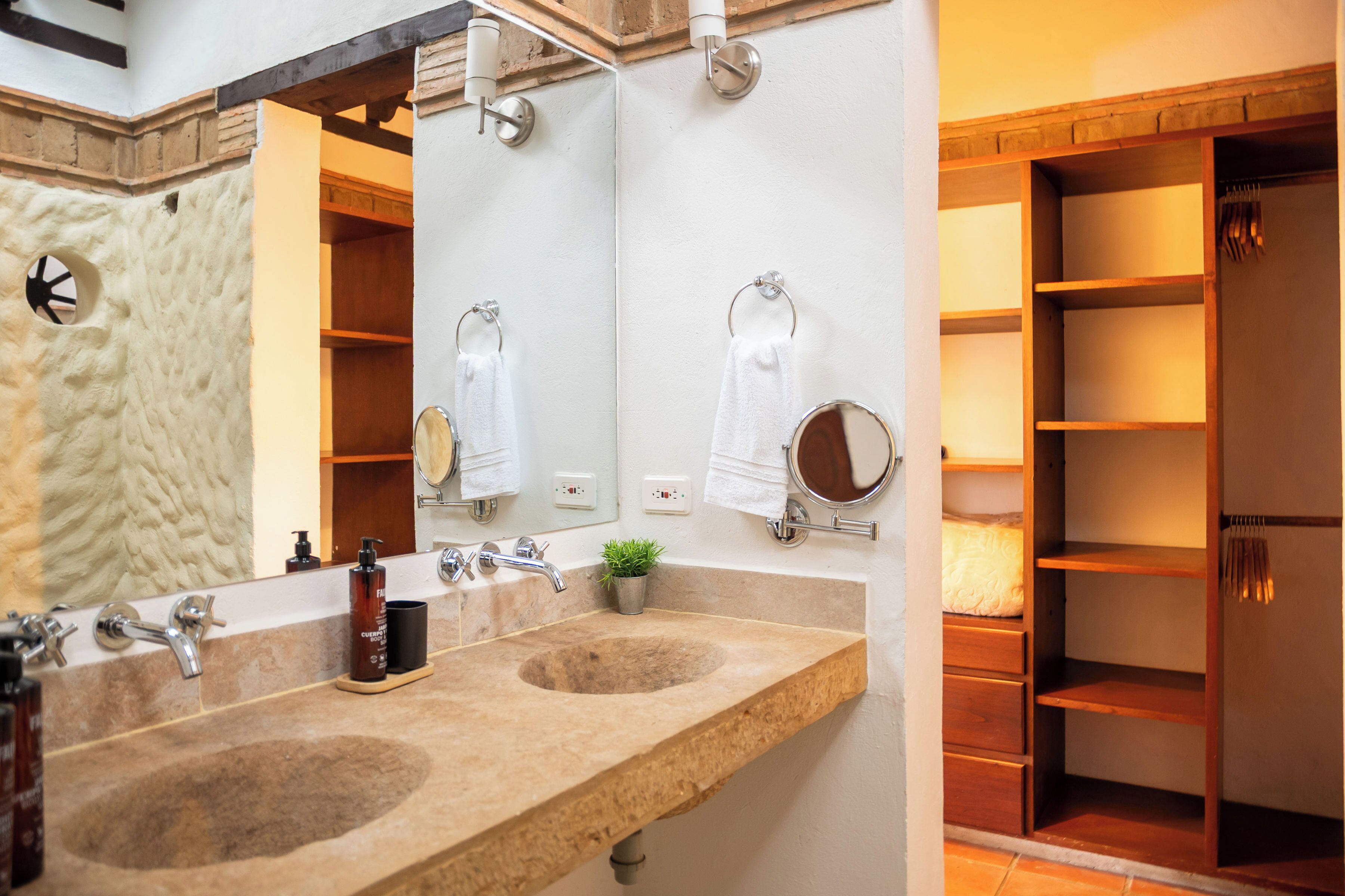 A bathroom with a double sink, a mirror, a towel rack, and a shelf with toiletries.