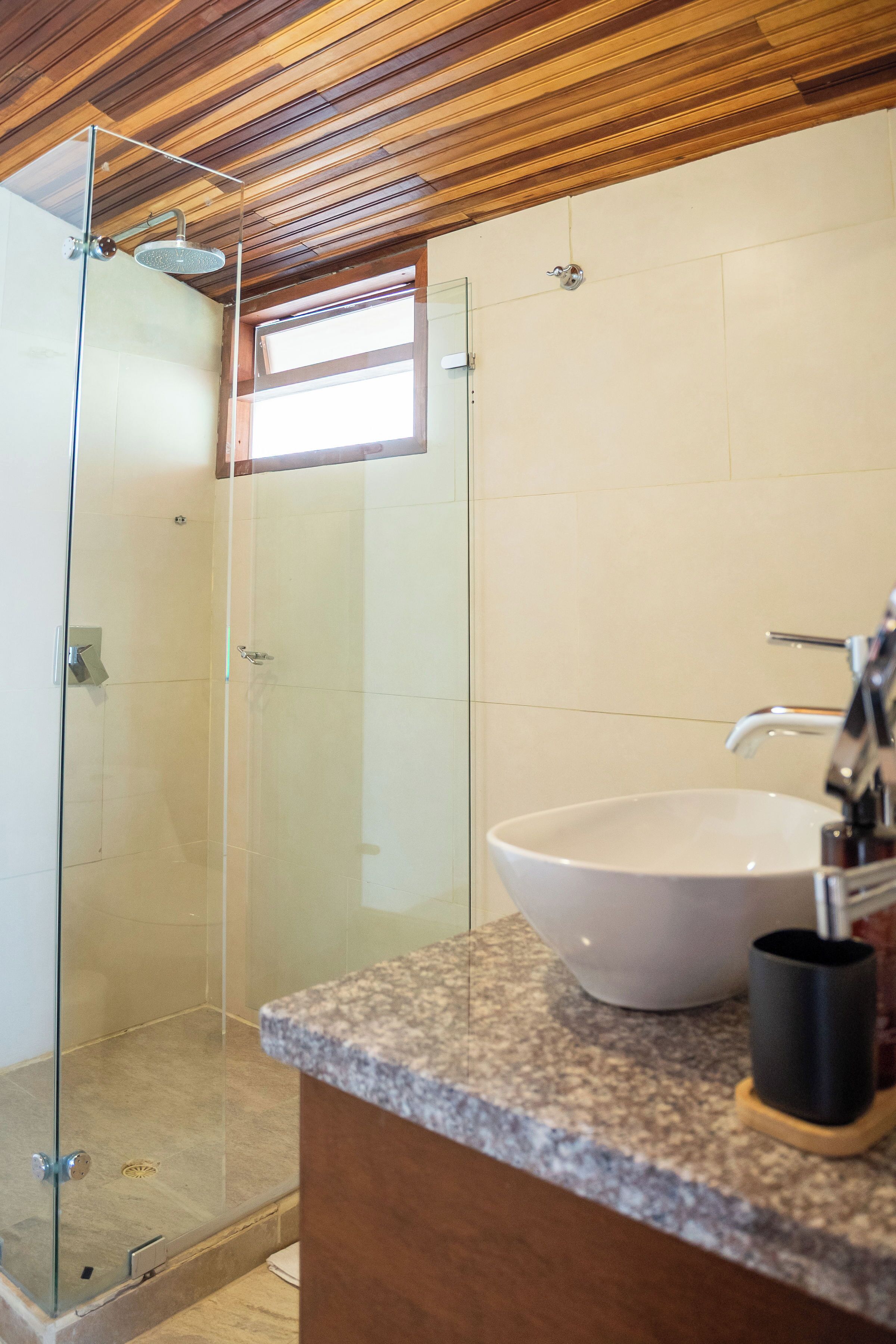 Un baño moderno con cabina de ducha de vidrio, un lavabo blanco y techo de madera.