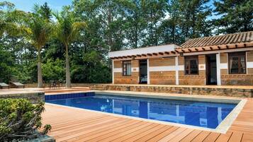 Zona junto a la piscina con una terraza de madera, una pileta y un edificio con tejado de tejas.