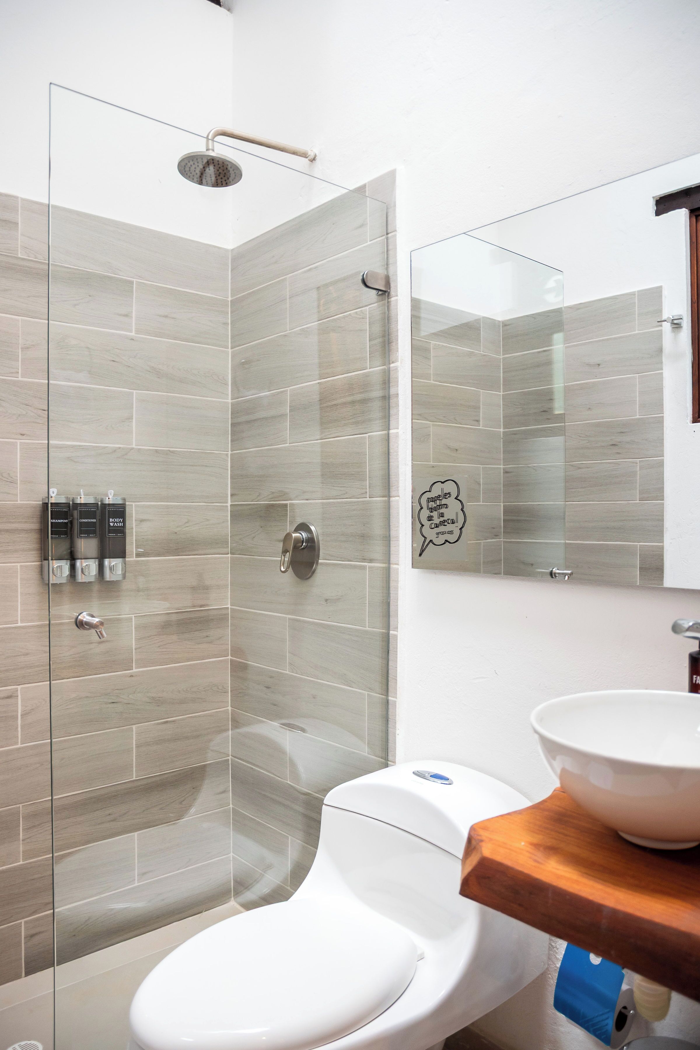 Un baño moderno con cabina de ducha de vidrio, inodoro y lavamanos con encimera de madera.