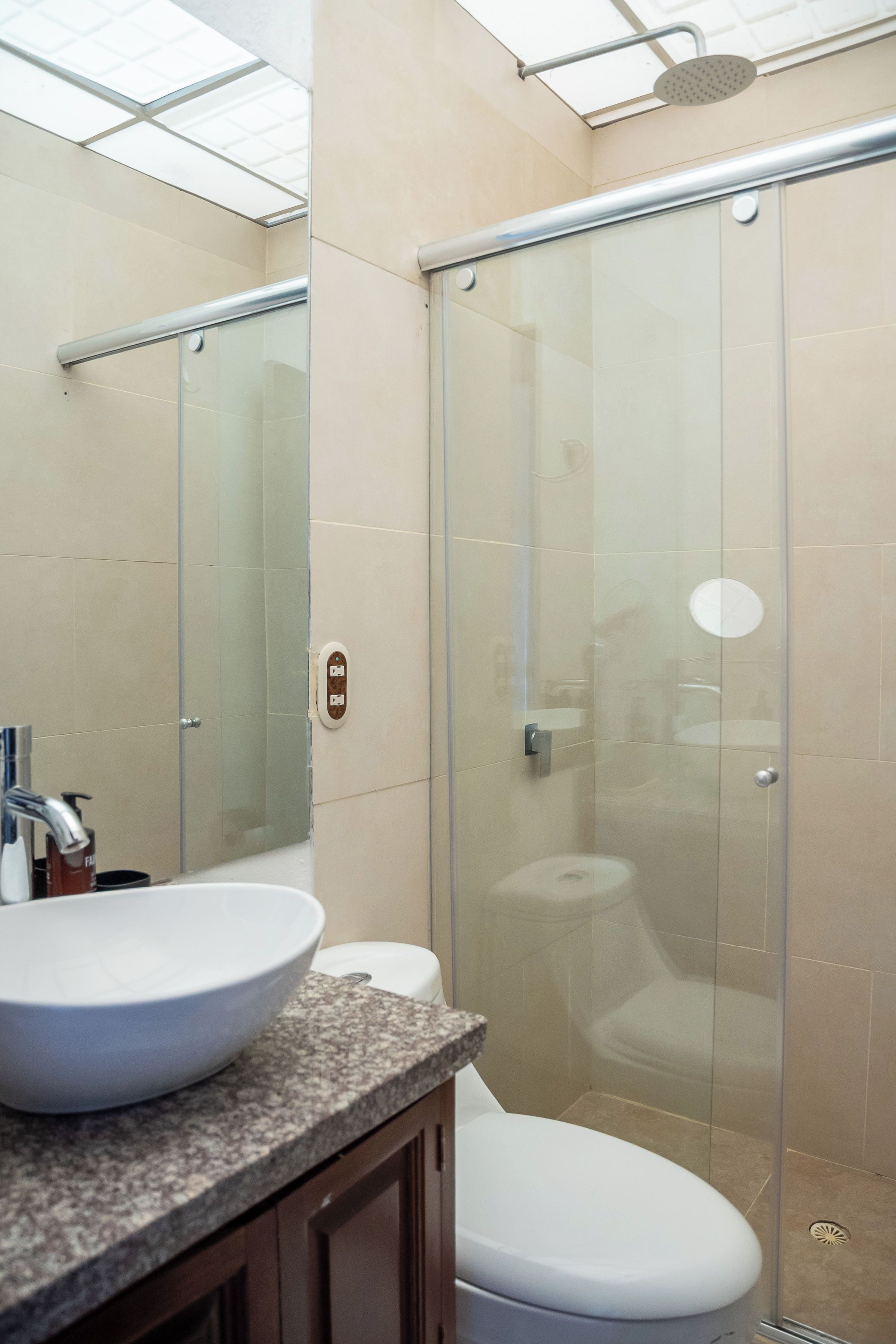 A bathroom with a glass-enclosed shower, a white sink, and a toilet.