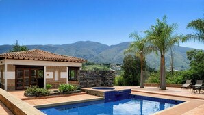 Una piscina con cubierta de madera, un pequeño edificio con techo de tejas y vistas a montañas.