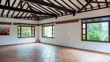 A spacious room with a tiled floor, wooden ceiling beams, and large windows with decorative frames.