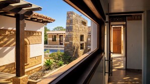 Vista a través de una ventana que muestra un edificio con una estructura de piedra, una piscina y una puerta de madera.