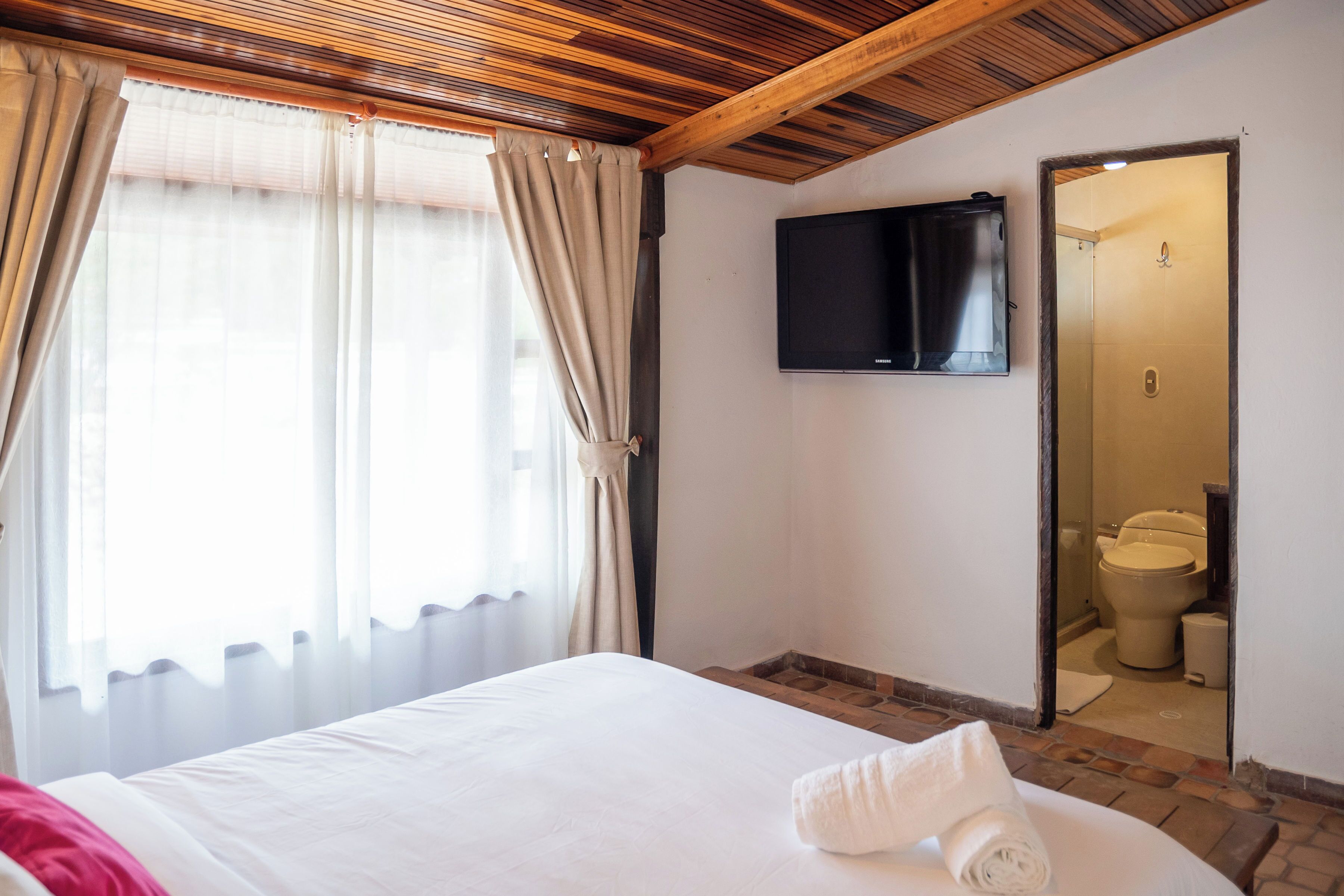A hotel room with a bed, a TV mounted on the wall, and a bathroom visible through an open door.