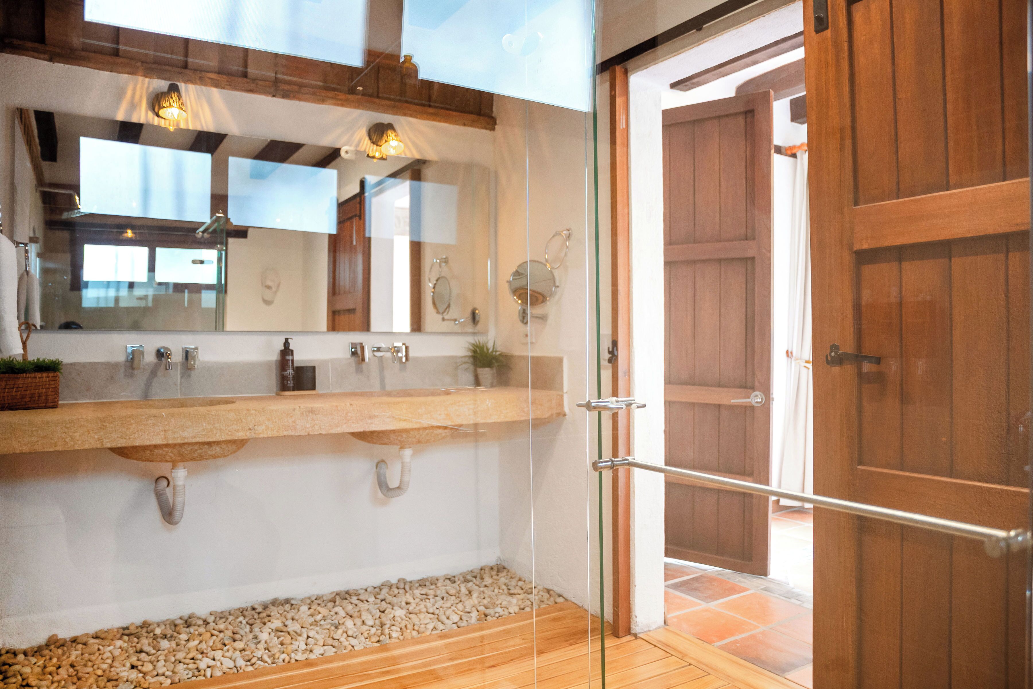 Un baño con un espejo grande, un tocador de madera, cabina de ducha de vidrio y una puerta de madera.