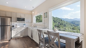 A modern kitchen with a large window offering a scenic mountain view. - Brand New Home- Maggie Valley Sunset (Waynesville)