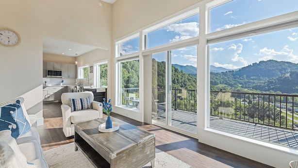 A spacious living room with a large window, a wooden coffee table, and a sofa. - Brand New Home- Maggie Valley Sunset (Waynesville)