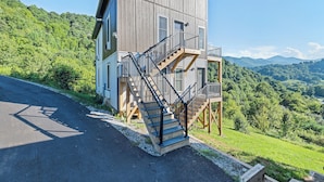 A two-story building with a wooden exterior, a staircase, and a view of a green valley. - Brand New Home- Maggie Valley Sunset (Waynesville)