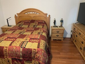 Une chambre à coucher avec un lit en bois, une table de chevet dotée de tiroirs, une commode et deux statuettes posées sur la table de chevet.