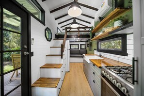 A compact kitchen with white cabinetry, a wooden countertop, and a gas stove. - Rural Oasis - Tiny Home | 2BR Cabin + Outdoor Firepit Experience (Palmwoods)