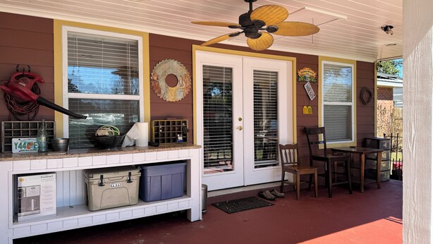 A porch with a ceiling fan, a table, chairs, a trash can, and a window with blinds.