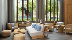 A modern living room with a sofa, chairs, and a coffee table. Large windows provide a view of greenery outside. - Mercure Rayong Lomtalay Villas and Resort (Klaeng)