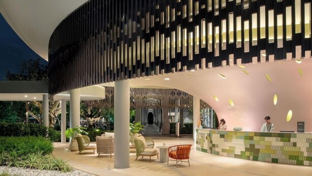 A modern hotel lobby with a curved reception desk, seating area, and a large, dark facade with vertical light panels. - Mercure Rayong Lomtalay Villas and Resort (Klaeng)
