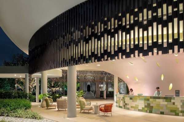 A modern hotel lobby with a curved reception desk, seating area, and a large, dark facade with vertical light panels. - Mercure Rayong Lomtalay Villas and Resort (Klaeng)