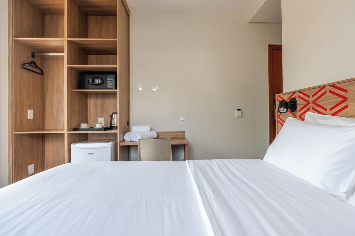 A hotel room with a bed, a desk, a kitchenette, and a wardrobe.
