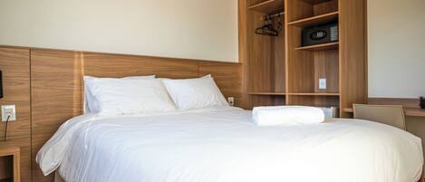 Una cama bien hecha con sábanas blancas, cabecera de madera y un armario empotrado de madera con estantes.